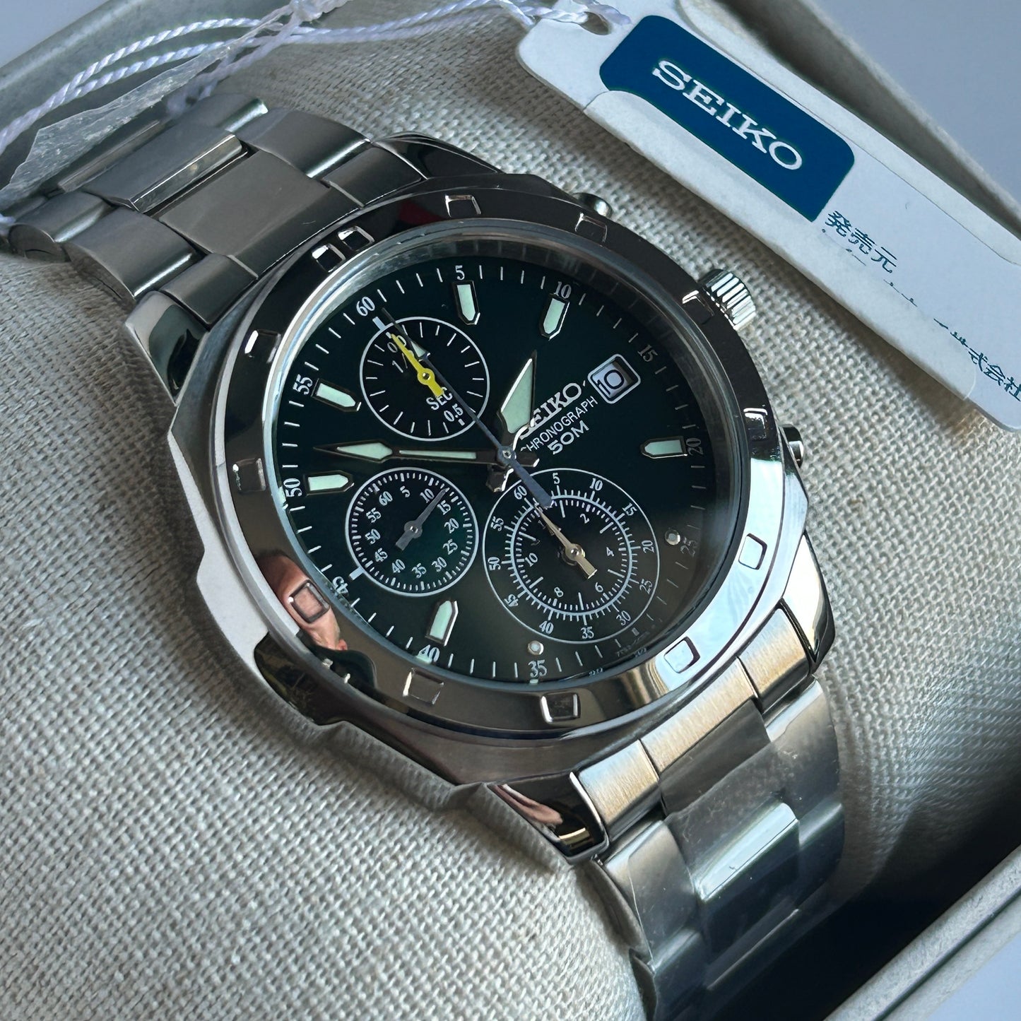 Seiko watch with a silver band and black face on a textured surface.