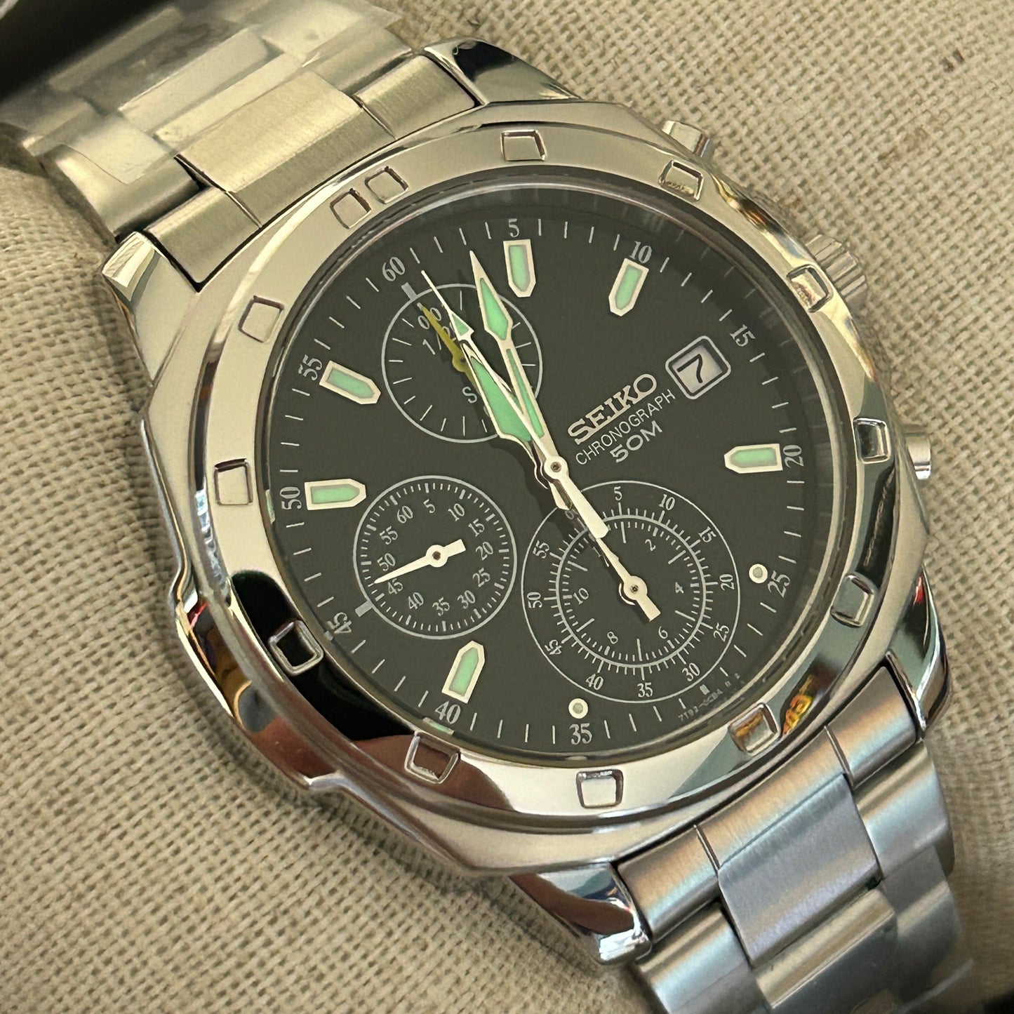 Silver Seiko watch with a black face on a textured beige background